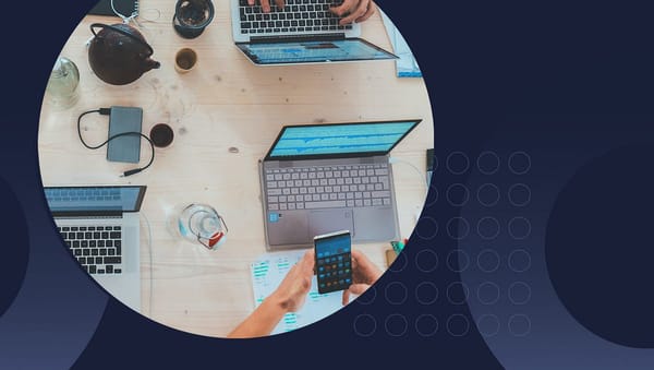 A desk with laptops, phones, note pads and a tea kettle to show that work is happening